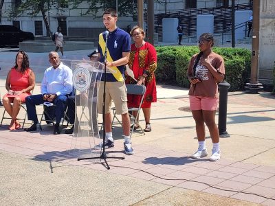 Left to right in background: Camden City Councilwoman Jannette; Camden Mayor Victor Carstarphen; Camden County Police Department Deputy Chief Brandon Kersey (face obstructed by speaker); CCP President & CEO Dana L. Redd

Left to right in foreground: Cairo Rivera; Monet High